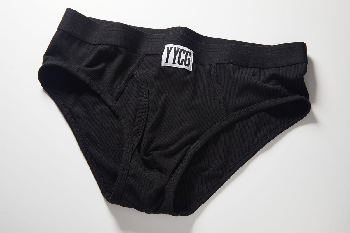 Black ribbed briefs with a white rectangular patch on the front waistband featuring the brand name 'YYCG' in black letters, laid flat on a white background.