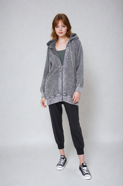Person wearing a gray hooded jacket and black pants on a white background
