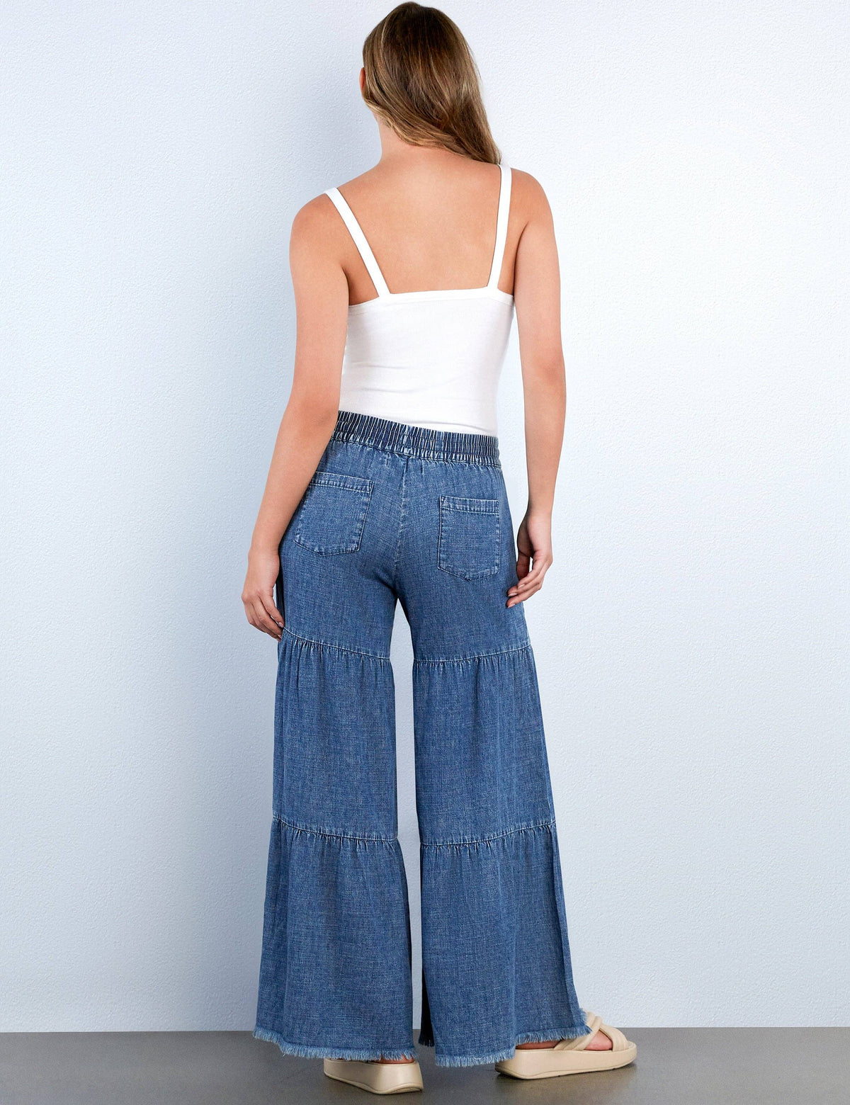 Woman wearing blue denim flared pants and a white top on a plain background