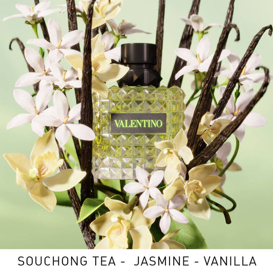 Valentino perfume bottle surrounded by vanilla beans and flowers on a light green background