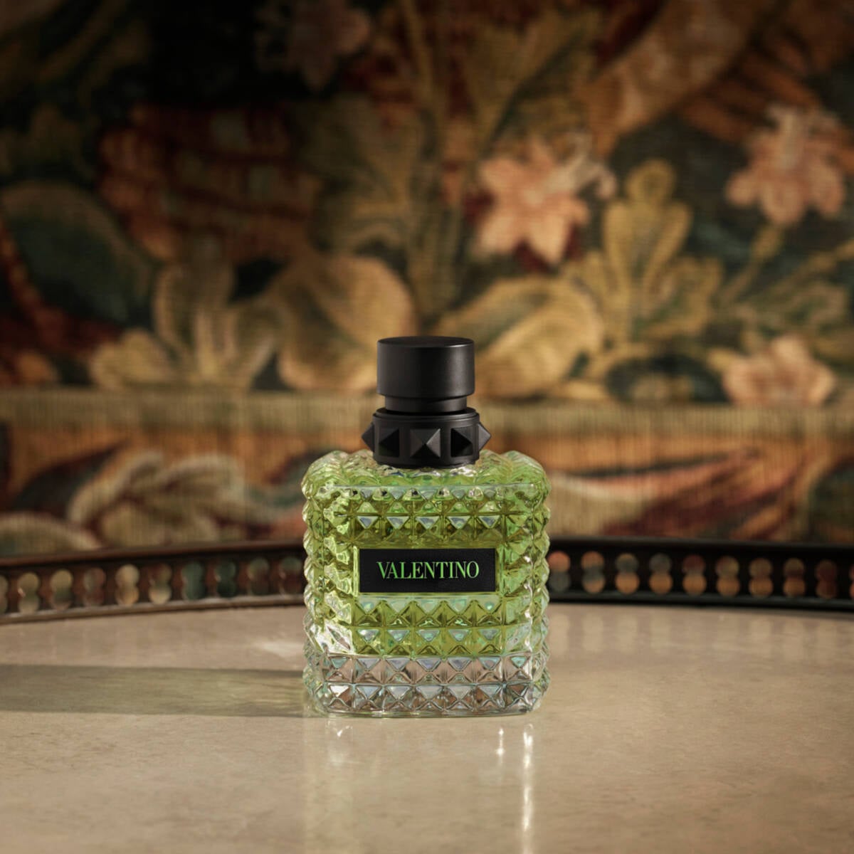 Valentino perfume bottle on a reflective surface with a decorative background