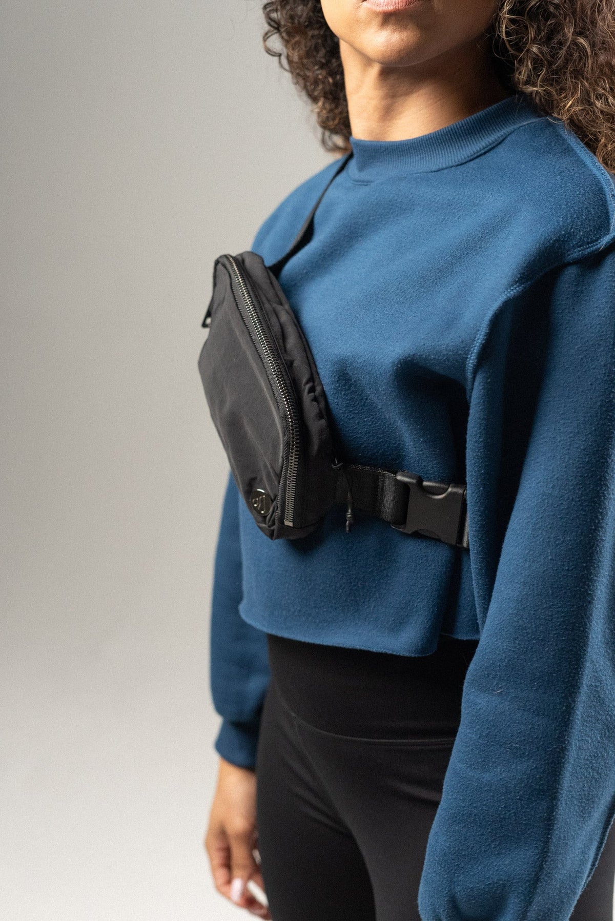 Person wearing a blue sweatshirt with a black fanny pack on a gray background