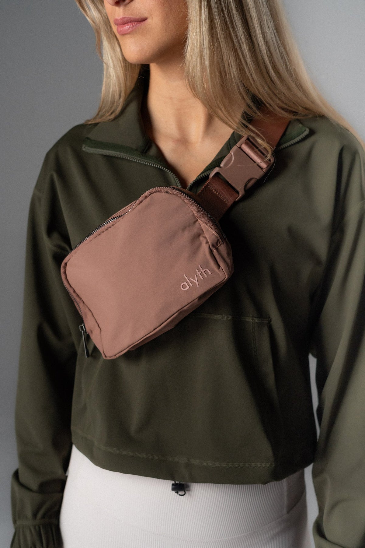 Person wearing a green jacket with a brown sling bag on a gray background