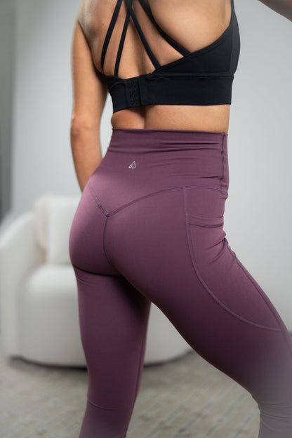 Person wearing purple leggings and black sports bra with a blurred background