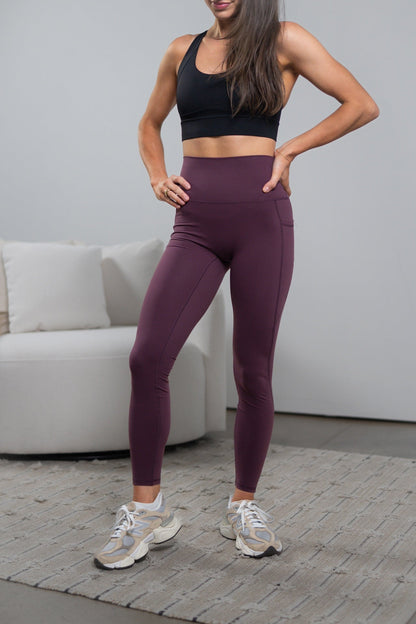 Woman wearing a black sports bra and purple leggings standing in a room with a white couch.