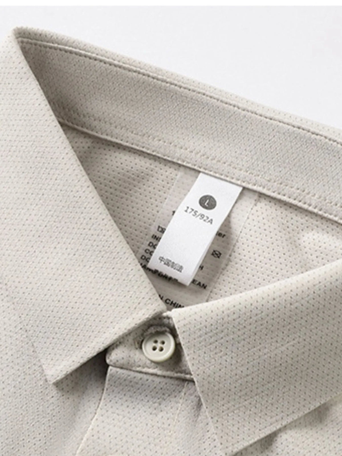 Close-up of a light gray textured shirt with a tag on a white background