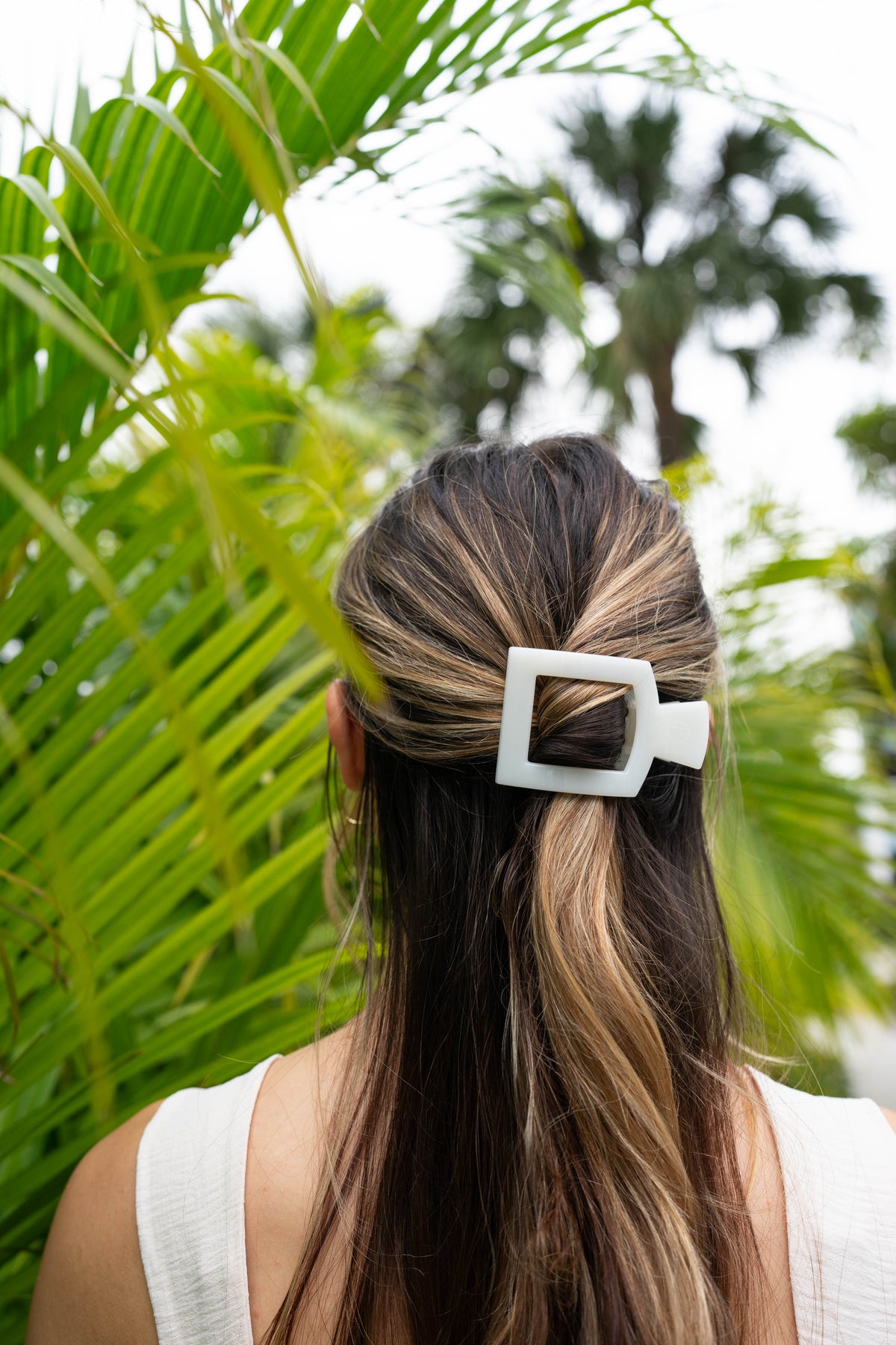 Person with a hair clip in a ponytail against a green leafy background