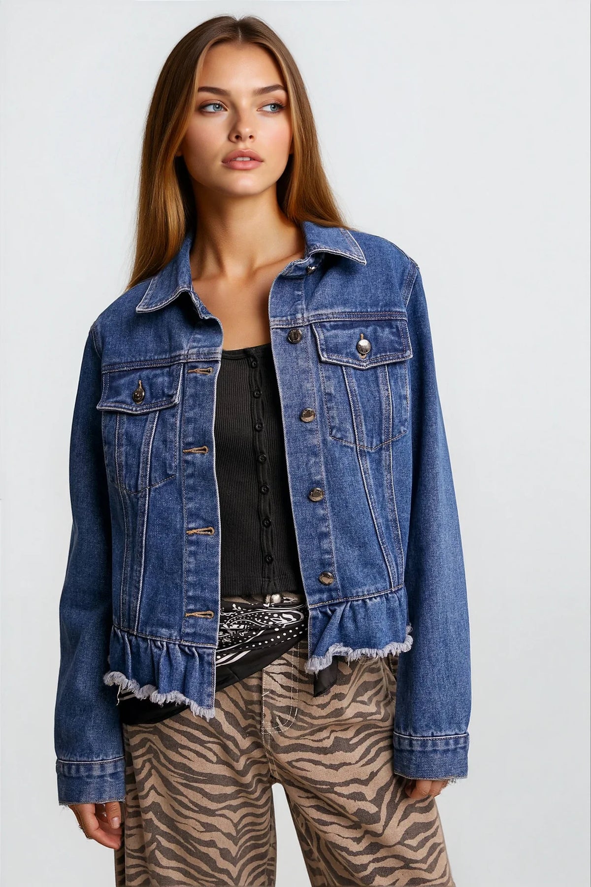 A woman modeling a cropped blue denim jacket with a raw, frayed hem, worn over a black top and paired with brown and beige zebra-print pants, against a light gray studio background.