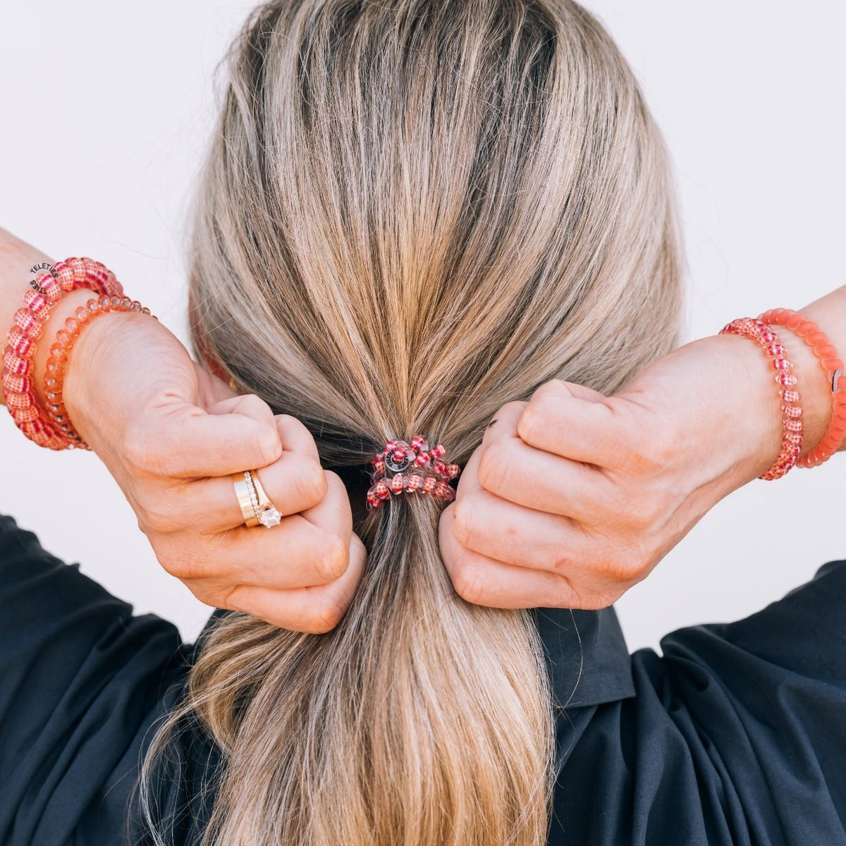 Person tying a hair tie with a pink floral design into a ponytail.