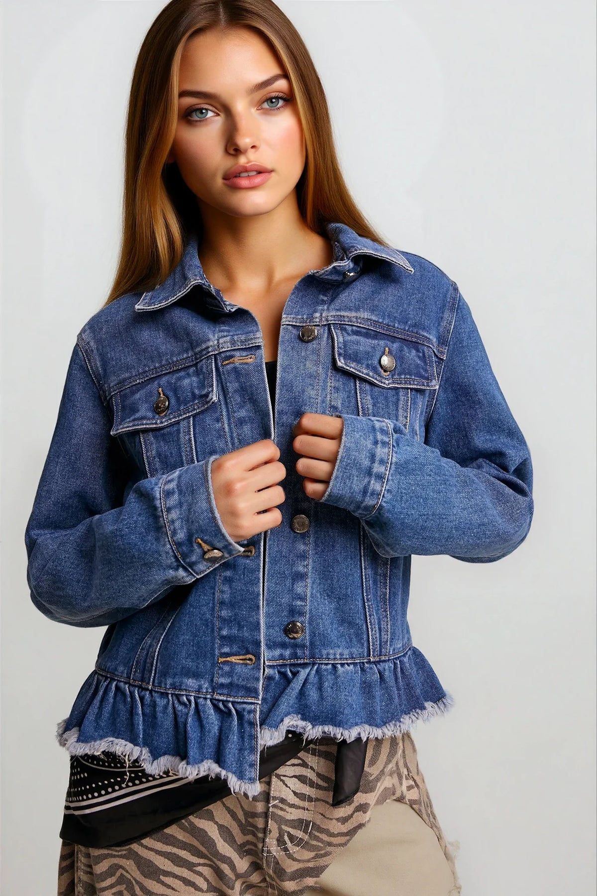 A woman wearing a cropped blue denim jacket with a ruffled hem, paired with beige zebra-print pants, against a light gray studio background.