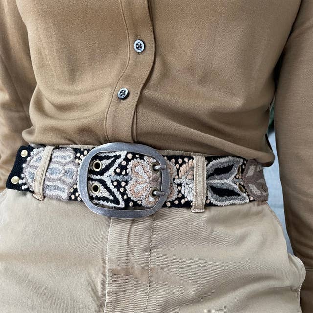 Close-up of a person wearing a beige shirt and beige pants with an ornate belt featuring a large silver buckle.