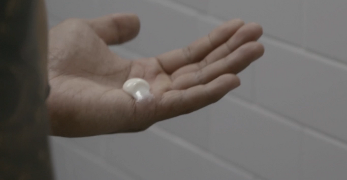 Hand holding a small white object against a tiled bathroom wall.