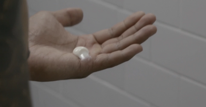 Hand holding a small white object against a tiled bathroom wall.