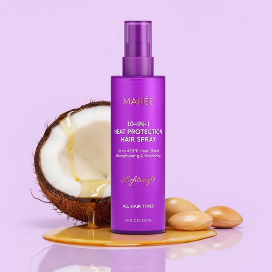 A purple bottle of MARÉE 10-in-1 Heat Protection Hair Spray stands on a reflective surface with a halved coconut, honey, and almonds beside it. The bottle label is white with purple text, and the background is a clean white studio setting.