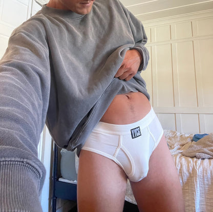Person wearing a gray sweatshirt and white underwear with a brand logo in a room.