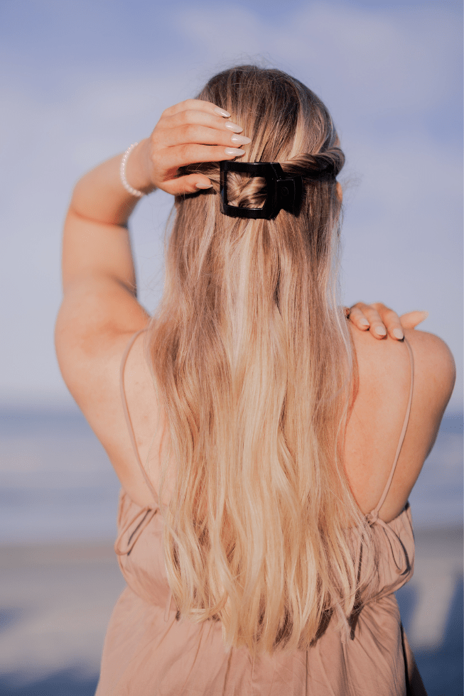 Person with long blonde hair wearing a black hair clip against a blurred natural background