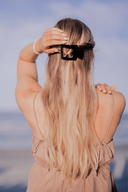 Person with long blonde hair wearing a black hair clip against a blurred natural background