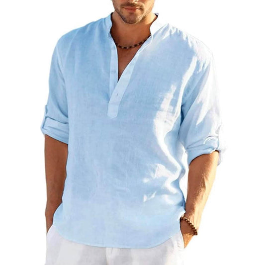 A man wearing a light blue linen henley shirt with rolled-up sleeves and white pants, shown from the chin down against a plain white background.