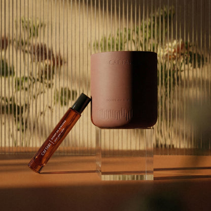 Brown candle and rollerball on a clear stand with blurred greenery in the background