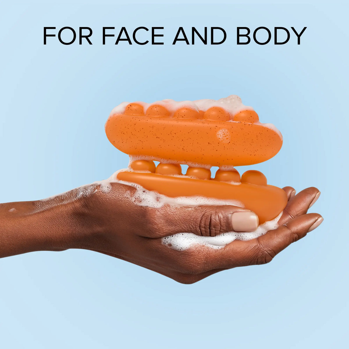 Orange bar of soap with bubbles on a hand against a light blue background, labeled 'For Face and Body'.