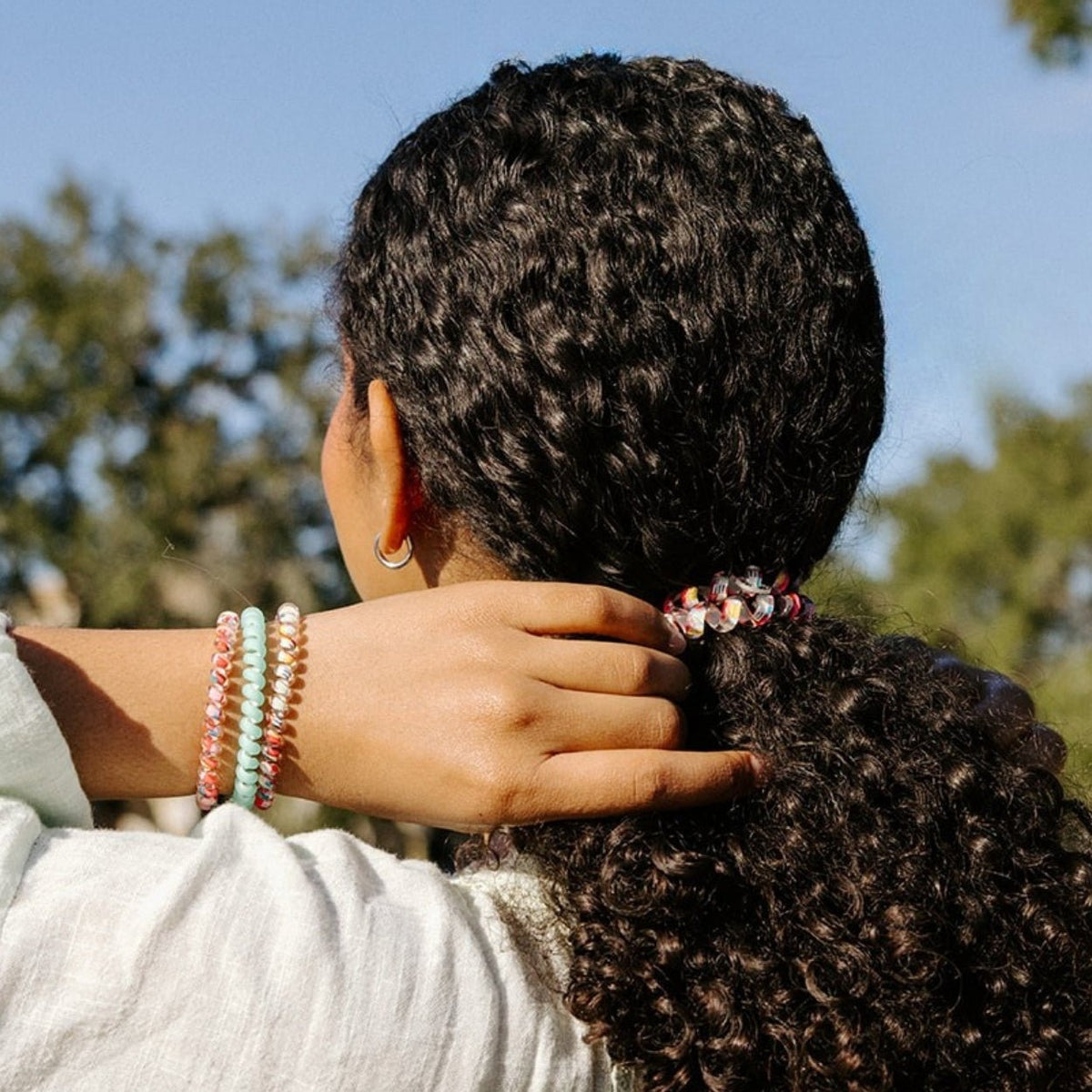 Person with braided hair wearing colorful bracelets, with a blurred natural background
