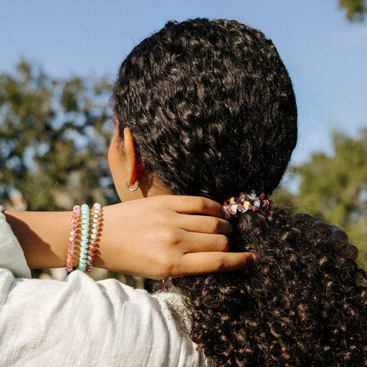 Person with braided hair wearing colorful bracelets, with a blurred natural background