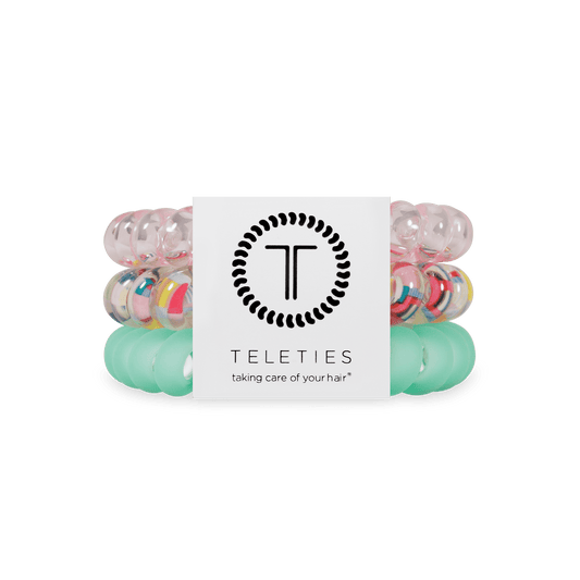 Three Teleties hair elastic bands stacked together with a white paper label in the center. The top band is translucent pink, the middle band is clear with multicolored confetti-like speckles, and the bottom band is translucent mint green.