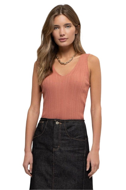 Woman wearing a pink ribbed tank top and black denim skirt on a white background