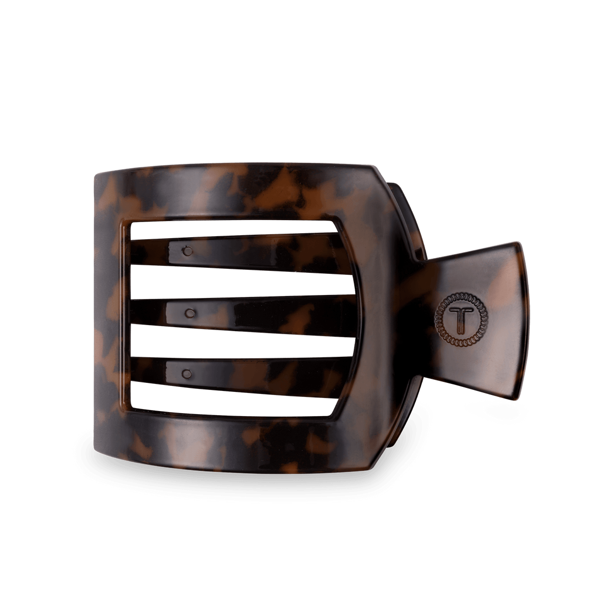 A wide, curved hair claw clip in a glossy tortoiseshell pattern, featuring a metal clasp with a circular 'T' logo, set against a solid dark green background.