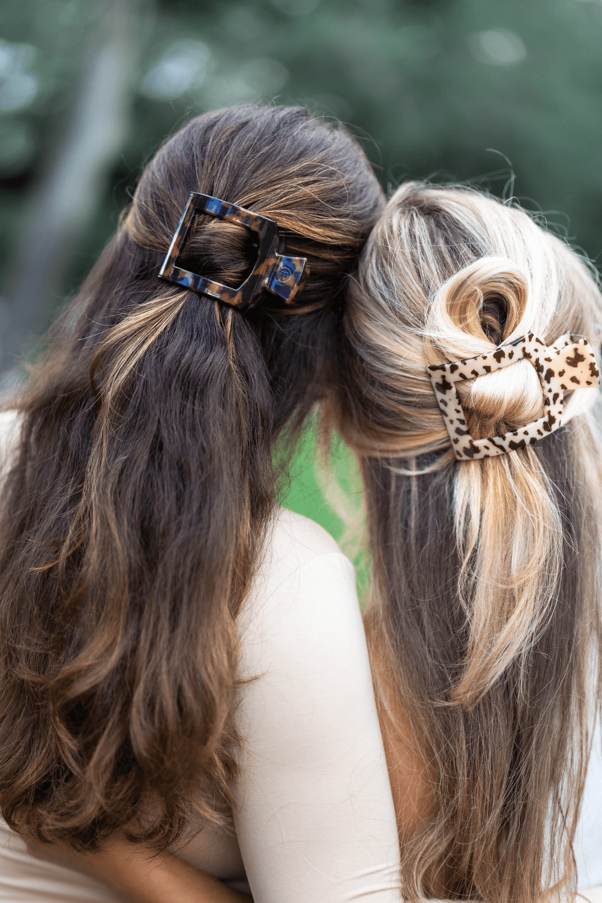 Two women with styled hair featuring decorative hair clips against a blurred natural background.