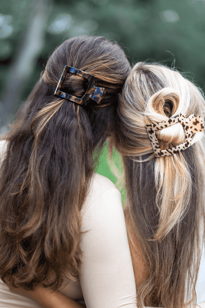 Two women with styled hair featuring decorative hair clips against a blurred natural background.