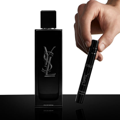 A hand holds a small black travel spray beside the full-size black Yves Saint Laurent MYSLF Eau de Parfum bottle with its silver YSL logo.